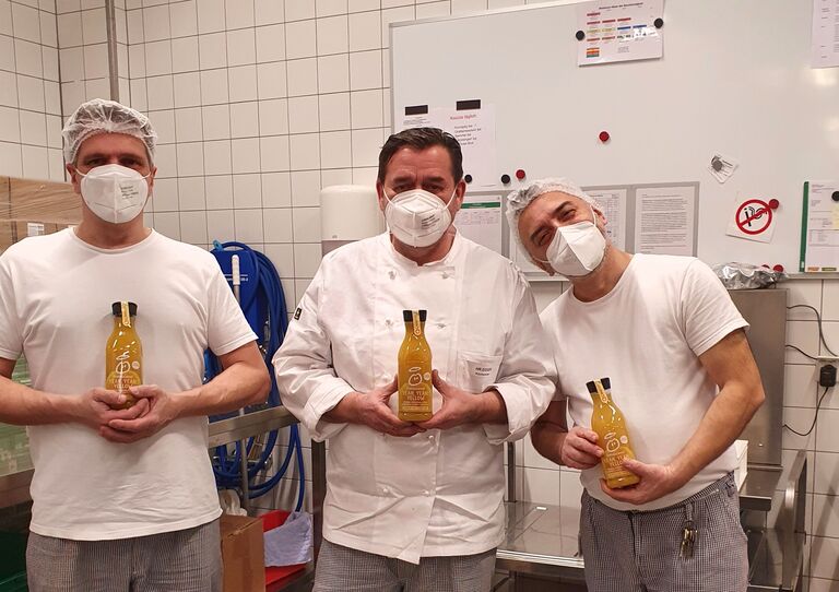 3 Mitarbeiter*innen aus der Küche stehen für ein Gruppenbild zusammen und halten jeweils eine Flasche Innocent Smoothie hoch.
