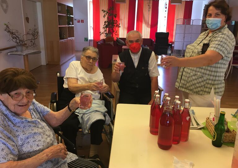 Bewohner*innen sitzen am Tisch und prosten sich mit Lavendelsirup zu. Eine Mitarbeiterin ist auch dabei.