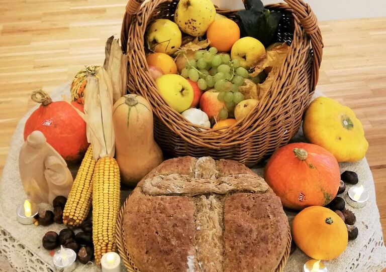 Ein Tisch mit Erntedank Dekoration, u.a. ein mit Obst gefüllter Korb, Mais und Kürbisse sowie selbst gebackenem Brot.