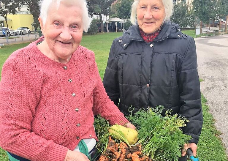 Zwei Bewohner*innen freuen sich über ihre Karotten-Ernte.