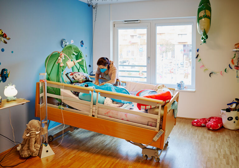 Eine Mitarbeiterin deckt einen Kunden in seinem Bett seines Einzelzimmer zu.