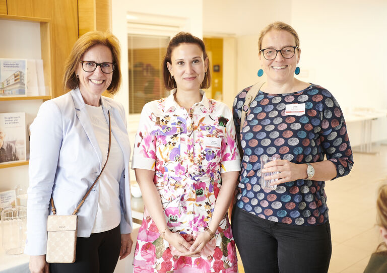 Drei Besucher*innen stehen einander und blicken in die Kamera