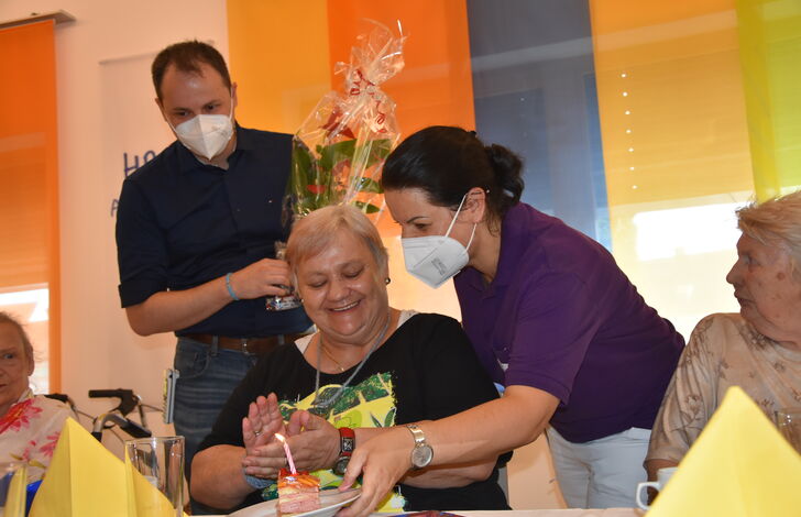Zwei Mitarbeiter*innen überreichen einer Bewohnerin ein Geburtstagsgeschenk.