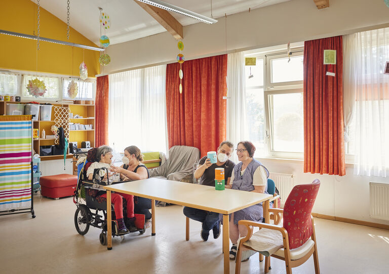 Kund*innen und Mitarbeiter*innen sitzen im Aufenthaltsraum und spielen mit Figuren.