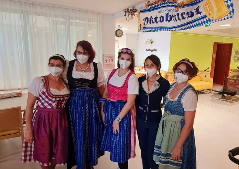 Mitarbeiterinnen aus dem Pflegekrankenhaus im Dirndl, hinter ihnen ein großes Schild mit der Aufschrift "Oktoberfest".