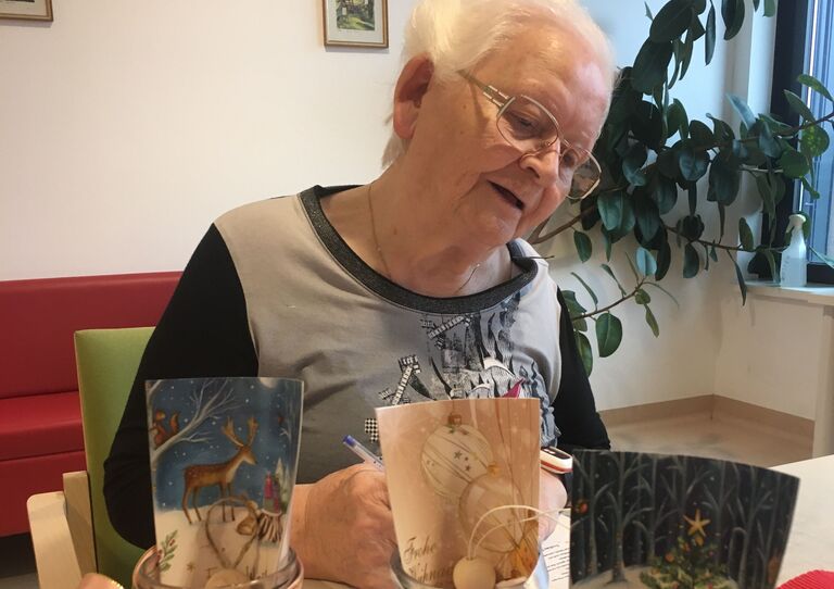 Eine Bewohnerin schreibt etwas auf einem Papier auf. Sie befüllt damit Gläser mit einer Weihnachtsbotschaft.
