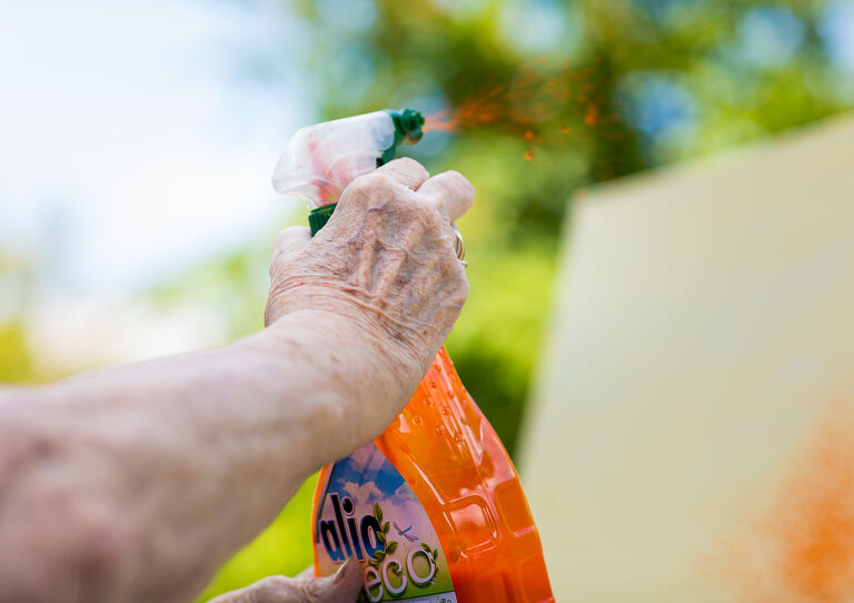 Die Hand einer Bewohnerin mit einer Sprühflasche und oranger Farbe.