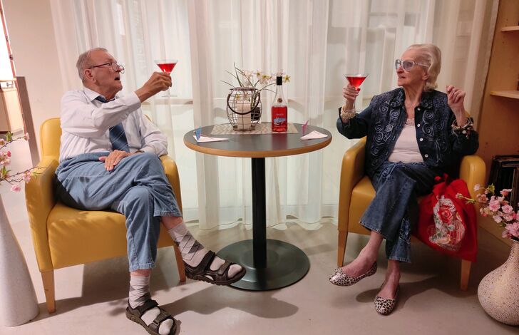 Eine Bewohnerin und ein Bewohner prosten sich zu.
