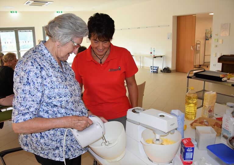Eine Bewohnerin mixt einen Teig, eine Seminarbäuerin schaut dabei zu.