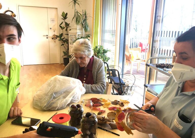 Eine Bewohnerin und zwei Mitarbeiter*innen basteln mit Laub