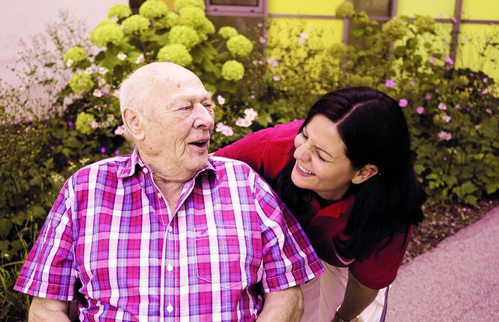 Pflegerin Tanja beugt sich über Bewohner Leopold, beide lachen.
