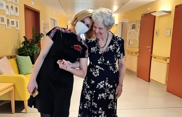 Eine Mitarbeiterin und eine Bewohnerin stehen Kopf an Kopf zusammen.