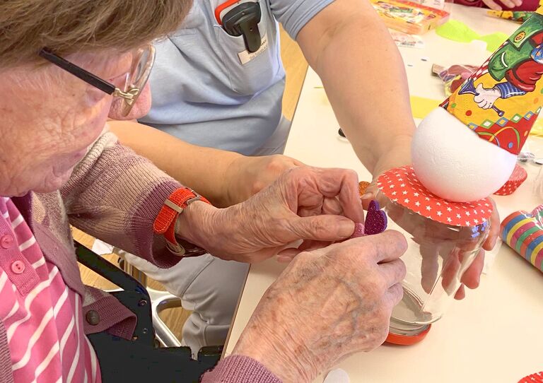 Mitarbeiterin und Bewohnerin basteln gemeinsam an einer Clownfigur.