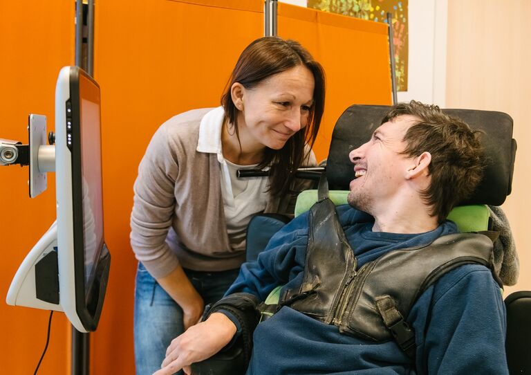 Betreuerin lächelt Kunde im Rollstuhl an.