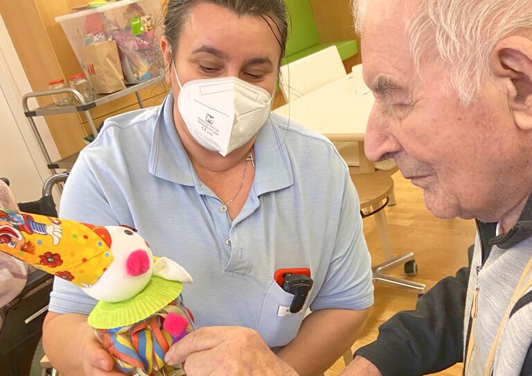 Mitarbeiterin und Bewohner basteln gemeinsam eine Clown-Figur.