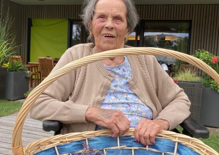 Bewohnerin hat einen Korb mit gepflückten Lavendel am Schoß. 