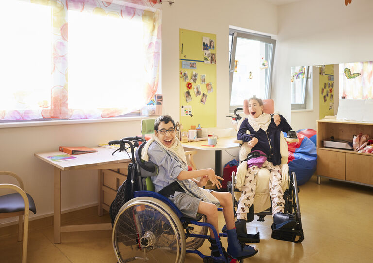 Ein Kunde und eine Kundin im Rollstuhl sitzen sich gegenüber und lächeln beide zur Kamera 