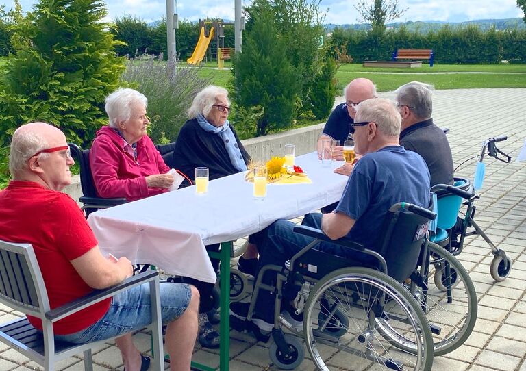 Einige Bewohner*innen aus dem Clementinum sitzen auf einem Tisch und plaudern miteinander