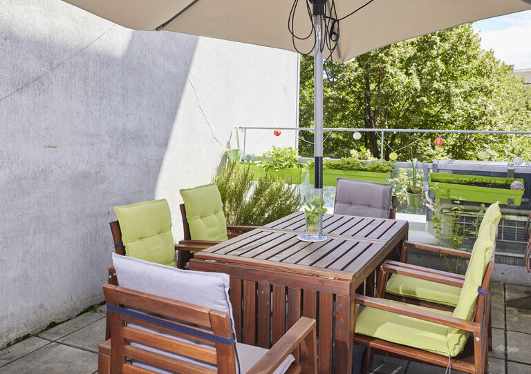 Terrasse der HABIT WG Arndtstraße mit Tisch und Sesseln mit grünen Polstern und großem Sonnenschirm