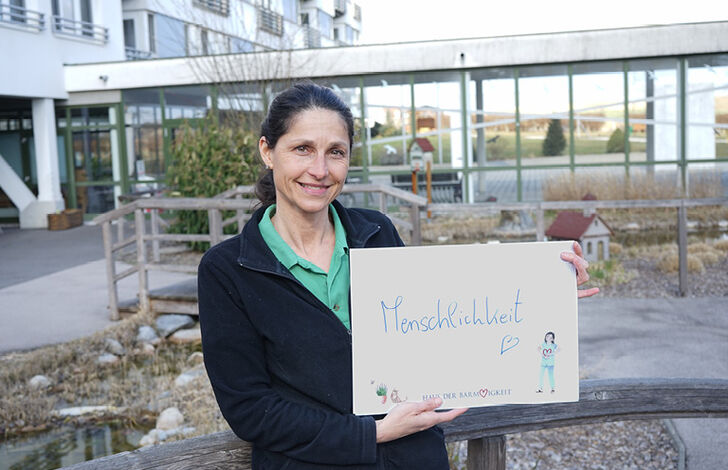 Mitarbeiterin hält Schild mit "Menschlichkeit"