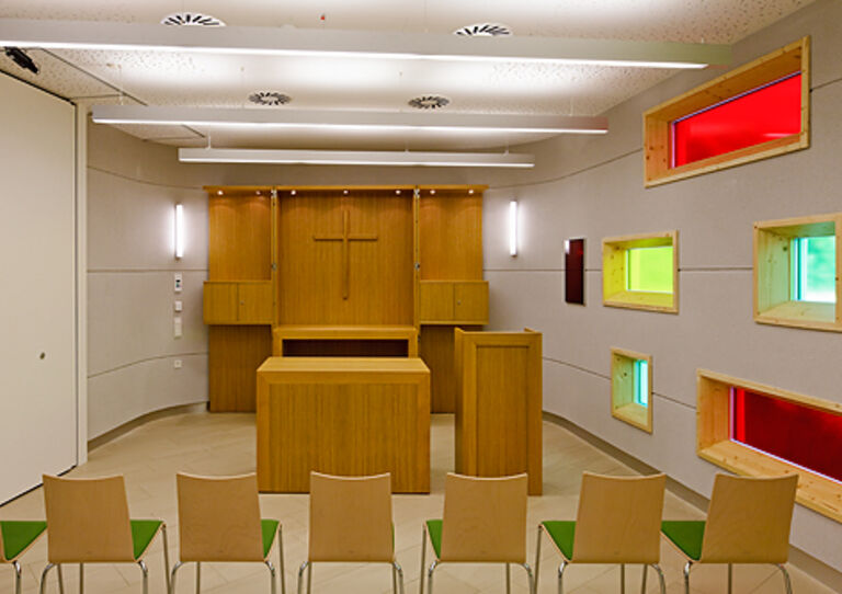 Die Kapelle des Urbanusheims mit einem Altar und Stühlen aus Holz sowie bunten Glasfenstern.