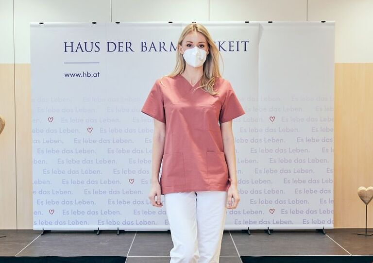 Eine Mitarbeiterin mit beerenfarbenem Oberteil auf dem Laufsteg.