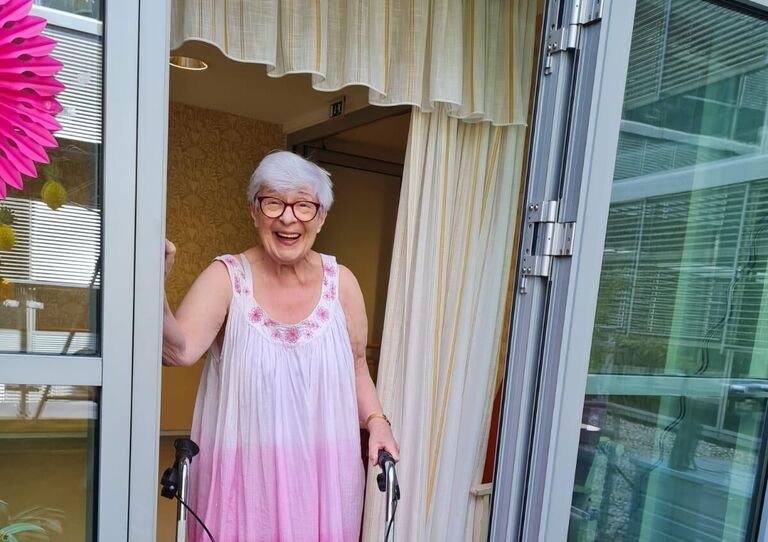 Bewohnerin steht mit Sommerkleid im Türstock