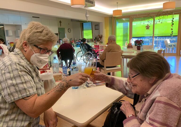 Eine Mitarbeiterin und eine Bewohnerin stoßen miteinander an.