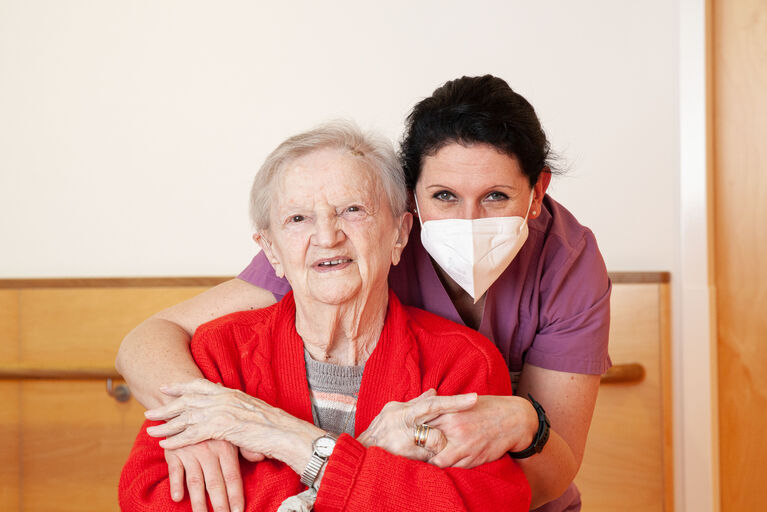 Mitarbeiterin Daniela umarmt Bewohnerin Elsa von hinten