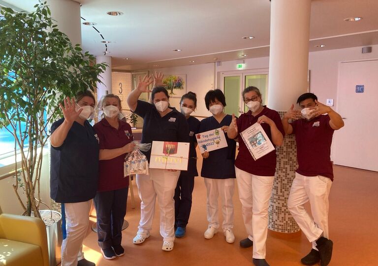 Sieben Mitarbeiter*innen halten ihre Hände in die Höhe und winken - sie halten einige Geschenke in die Höhe.