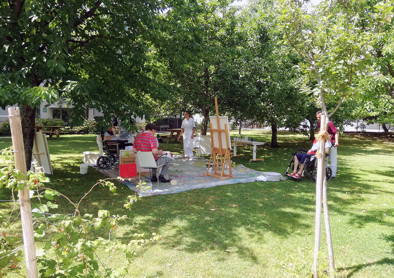 Eine Gruppe von Bewohner*innen beim Action Painting im Garten.
