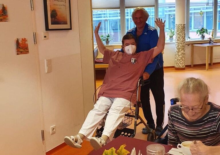 Zwei Kolleg*innen lachen miteinander, eine Bewohnerin auch und ein Kollege sitzt spaßhalber im Rollstuhl.