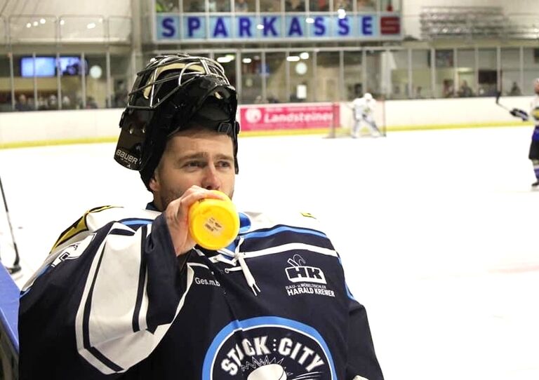 Vladimir Oleksak ist in voller Eishockeymontur im Eishockeystadion und trinkt aus einer Wasserflasche.