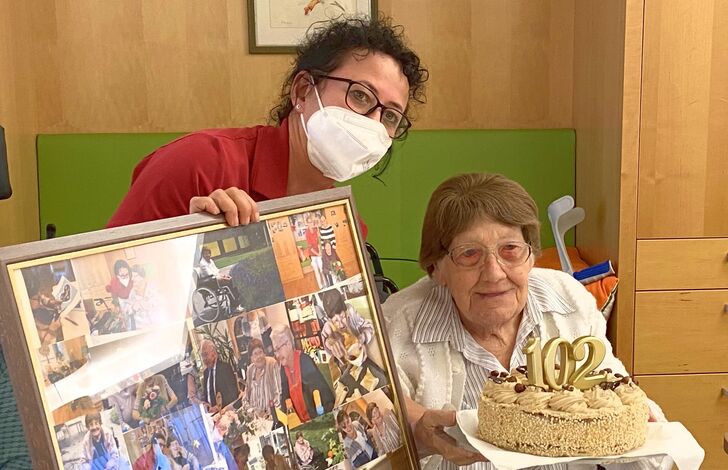 Eine Mitarbeiterin überreicht einer Bewohnerin zum 102. Geburtstag eine Bildercollage.