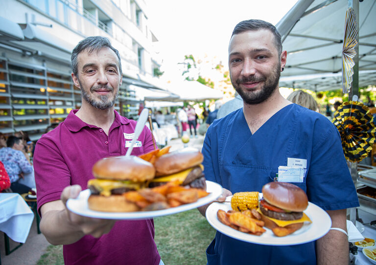 Zwei Mitarbeiter präsentieren ihren Burger mit Pommes.