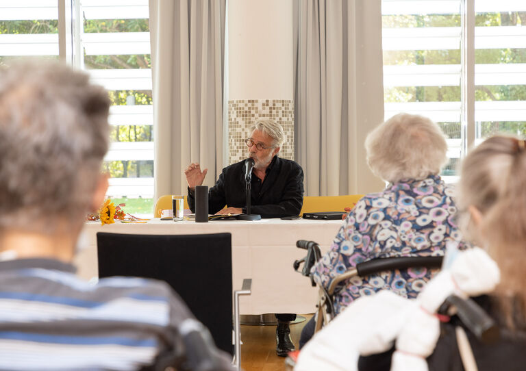 Adi Hirschal singt ganz vorne - Aufnahme von einigen Bewohner*innen von hinten.