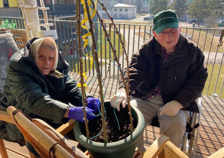 Eine Bewohnerin setzt die Frühlingsblumen ein und ein Bewohner hilft ihr dabei. 
