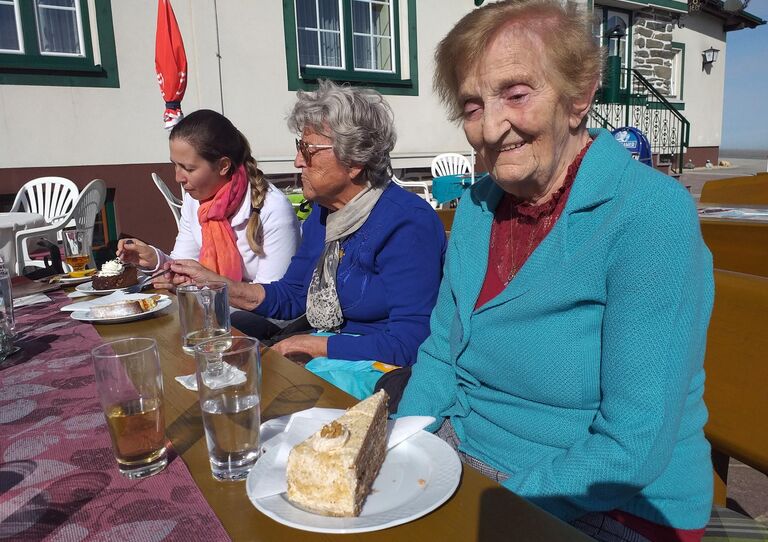 Zwei Bewohnerinnen und die Seniorenbetreuerin essen einen Kuchen in der Sonne.