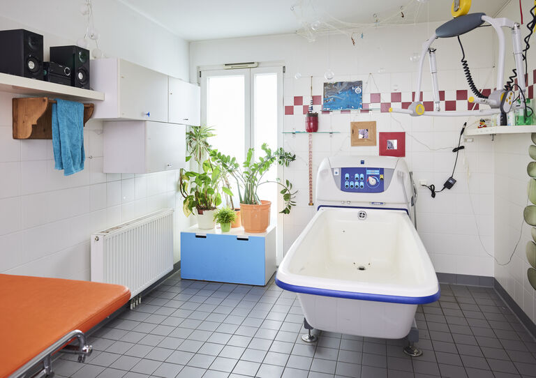 Pflegebad der HABIT WG Thürnlhofstraße mit oranger Liege im Vordergrund und Pflanzen am Fenster