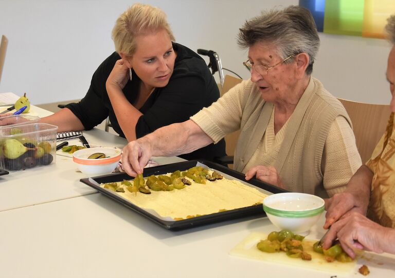 Eine Bewohnerin schneidet Obst und erzählt dabei von früher, eine Seminarbäuerin hört zu und macht Notizen.