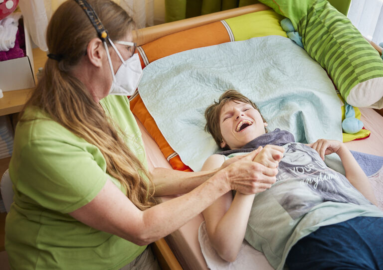 Eine Mitarbeiterin hält die Hand einer Kundin, die gerade im Bett liegt lacht.