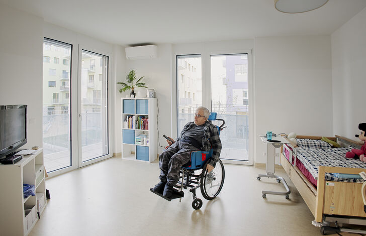 Ein Einblick in ein Zimmer des neuen HABIT Garconnierenverbundes in der Ilse-Buck-Straße, darauf zu sehen ist ein Bewohner im Rollstuhl.