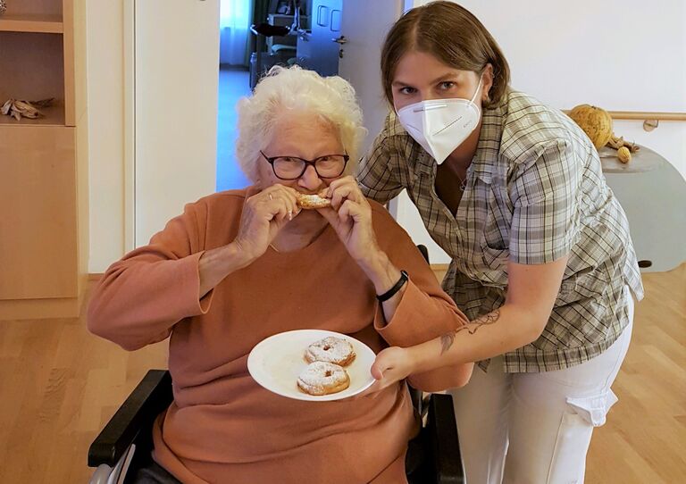 Eine Bewohnerin probiert einen Apfelring, eine Mitarbeiterin hält den Teller.