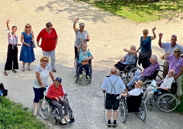 Ein Gruppenbild mit Bewohner*innen und Mitarbeiter*innen, die in die Kamera winken.