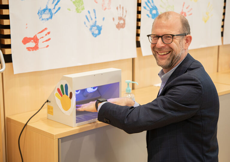 HB Geschäftsführer untersucht seine Hände mit Blaulicht.