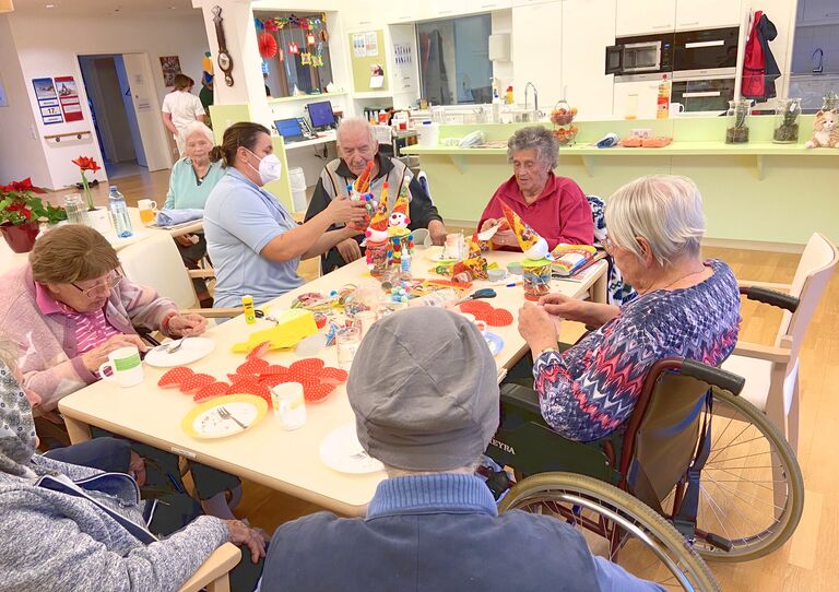 Bewohner*innen und eine Mitarbeiterin basteln rund um einen Tisch.