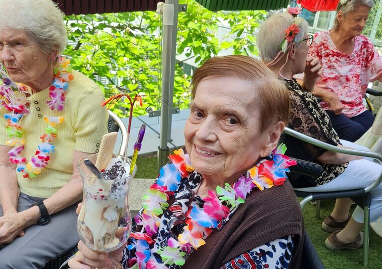 Bewohnerin hält einen Eiskaffee in der Hand, sie trägt eine Blumenkette