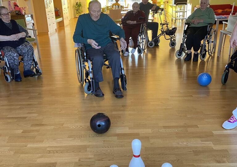 Der Ball, den ein Bwohner gerade geworfen hat, macht sich auf den Weg zu den Kegeln.