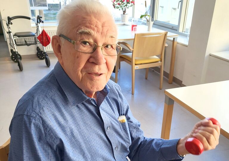 Bewohner trainiert mit Hantel und blickt in die Kamera.