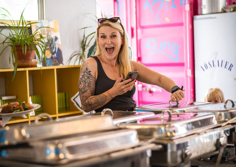 Eine Mitarbeiterin holt sich gerade am Buffet etwas zu essen und lächelt lustig in die Kamera.